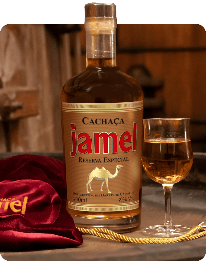 Garrafa de Cachaça Jamel Reserva Especial em primeiro plano com um copo cheio ao lado e um pano de veludo vermelho, sobre um balcão de madeira, indicando o ambiente refinado de sua degustação.